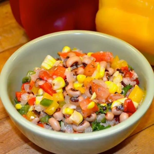 A light green bowl filled with a colorful black-eyed pea salad, corn, and diced bell peppers.