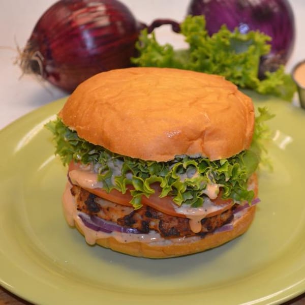 Lola's Chicken Shack fried chicken sandwich with lettuce, tomato, onion, and sauce on a green plate.