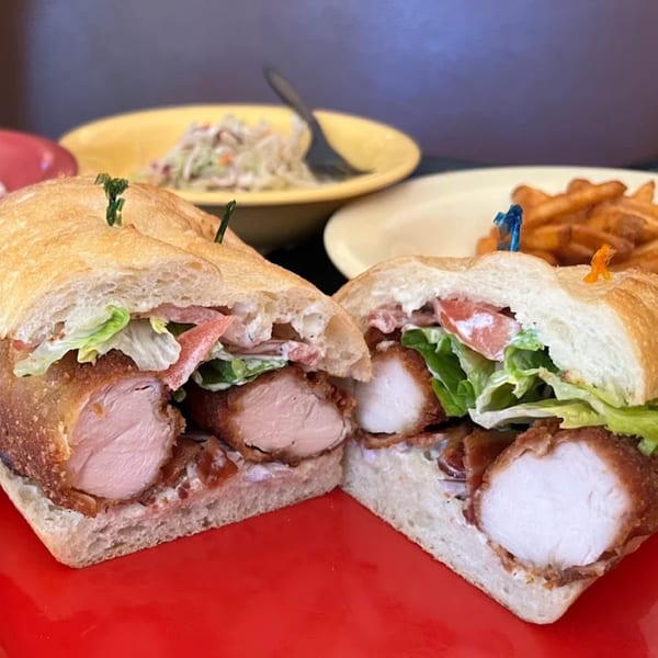 Lola's Chicken Shack fried chicken sandwich, cut in half, with lettuce, tomato, and coleslaw.